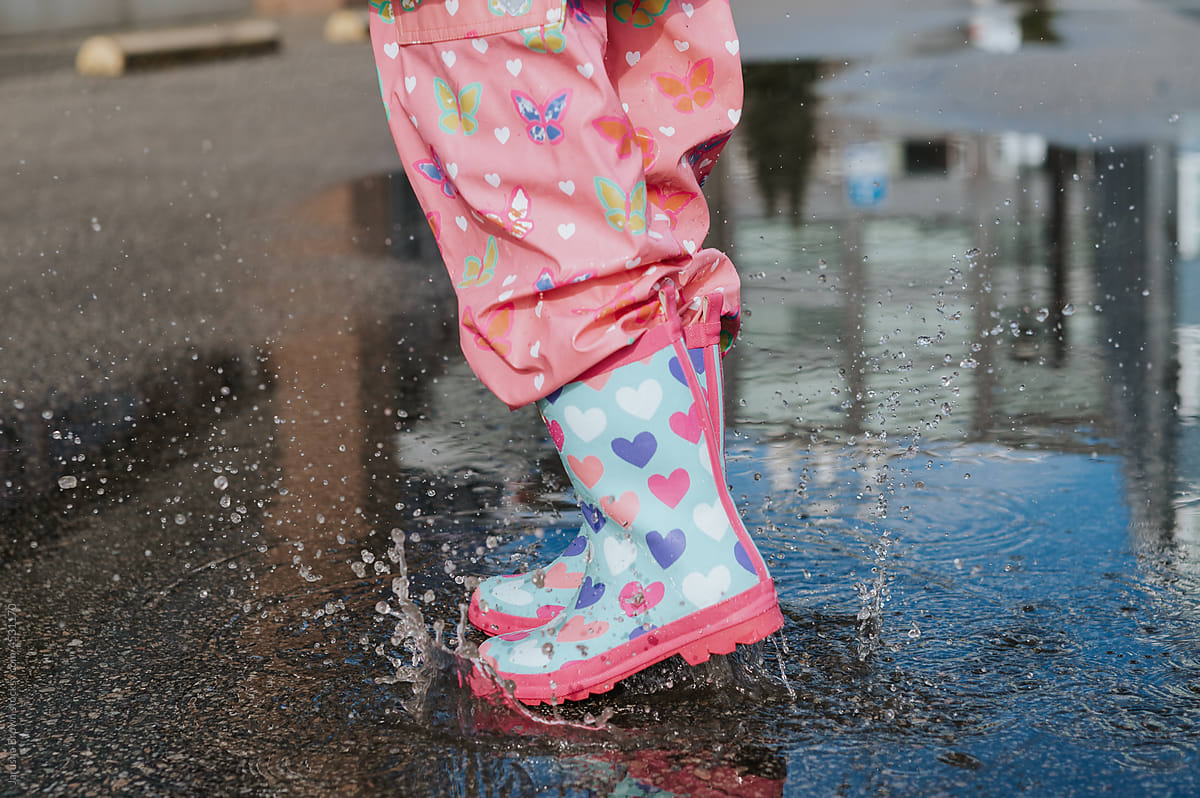Closeup photo of colourful rain boots splashing in a puddle.