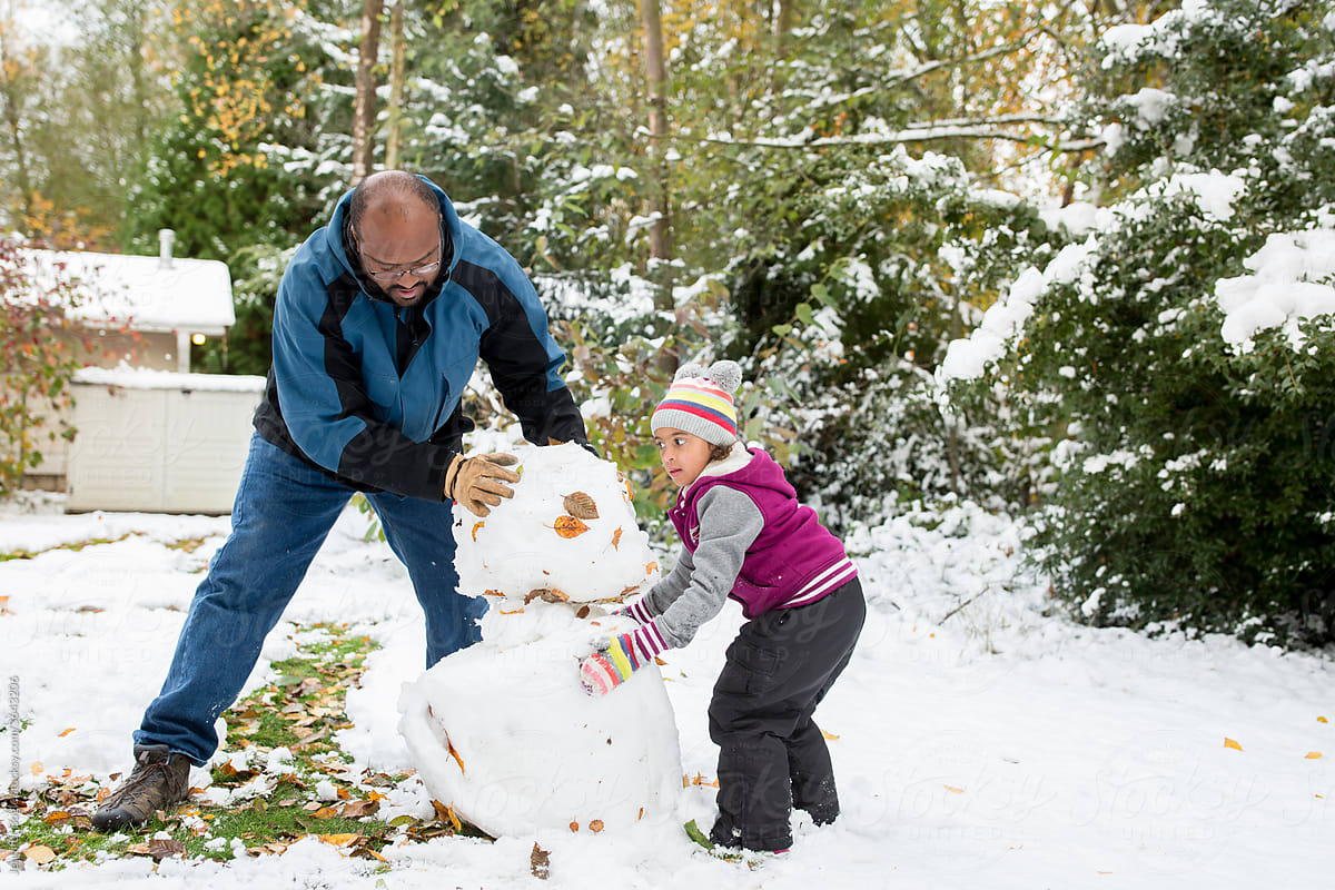 Father and daughter build snowman in back yard