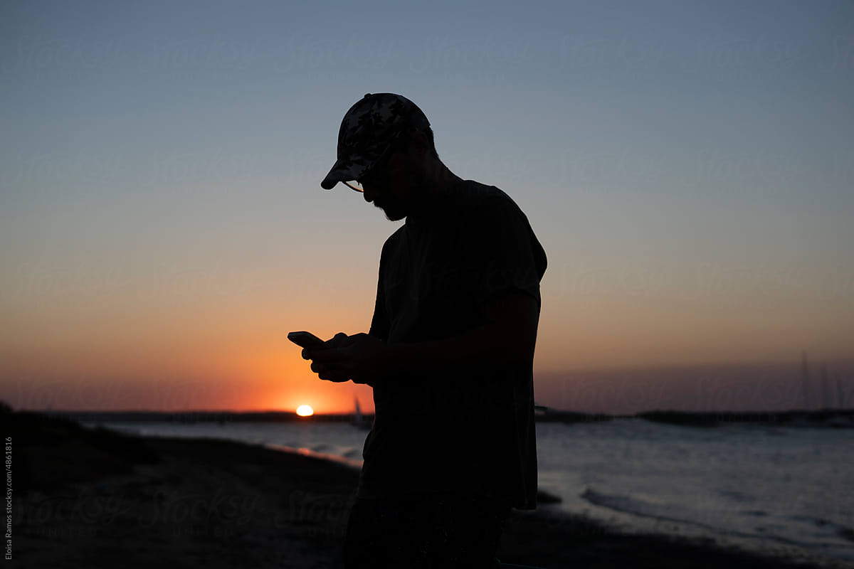 Man checking phone at the beach during sunset