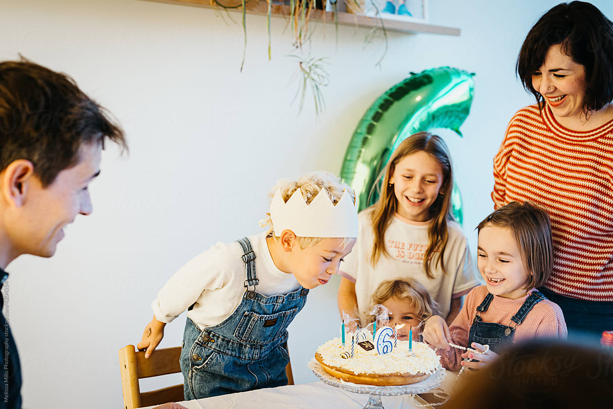 Boy blowing candles on a birthday cake together with family friends
