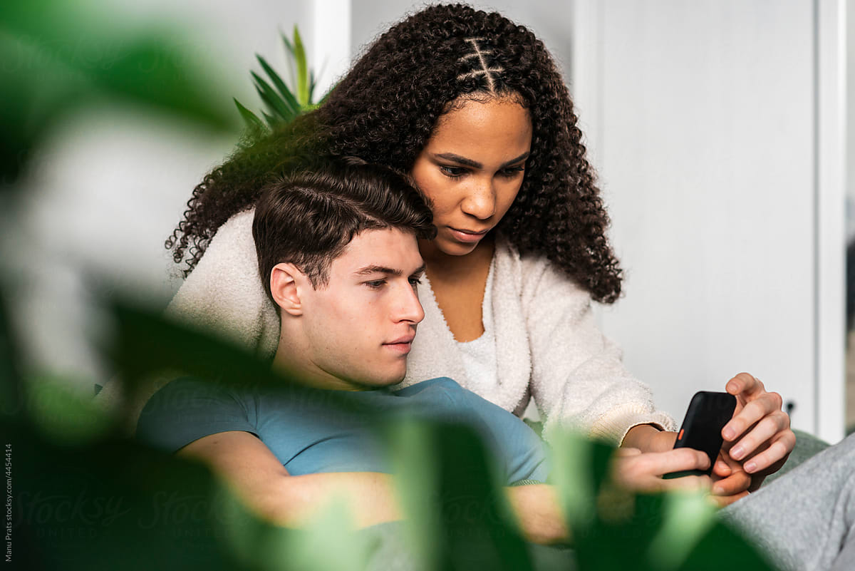 Multiracial couple browsing smartphone together on bed
