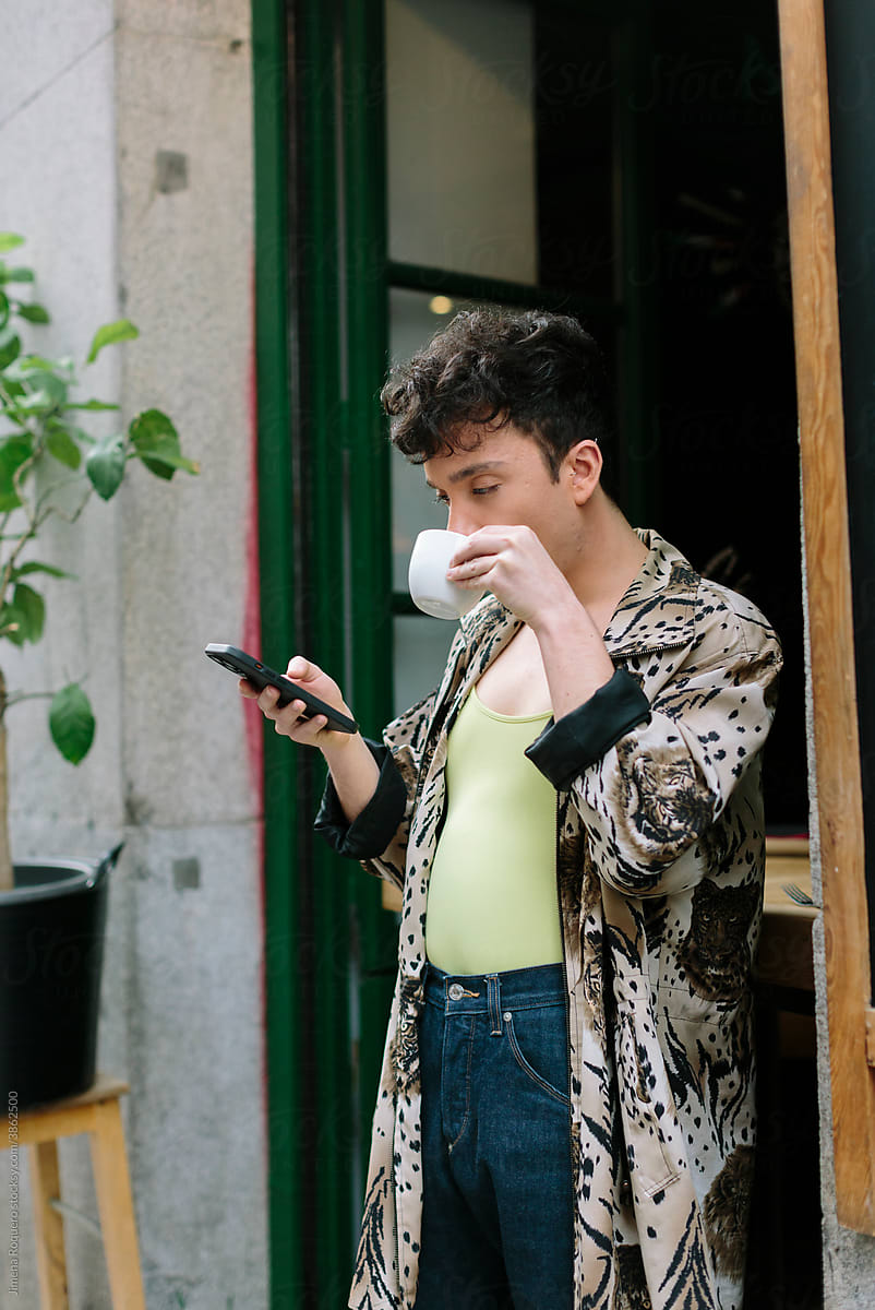 Young extravagant gay man outside a city cafeteria checking his phone