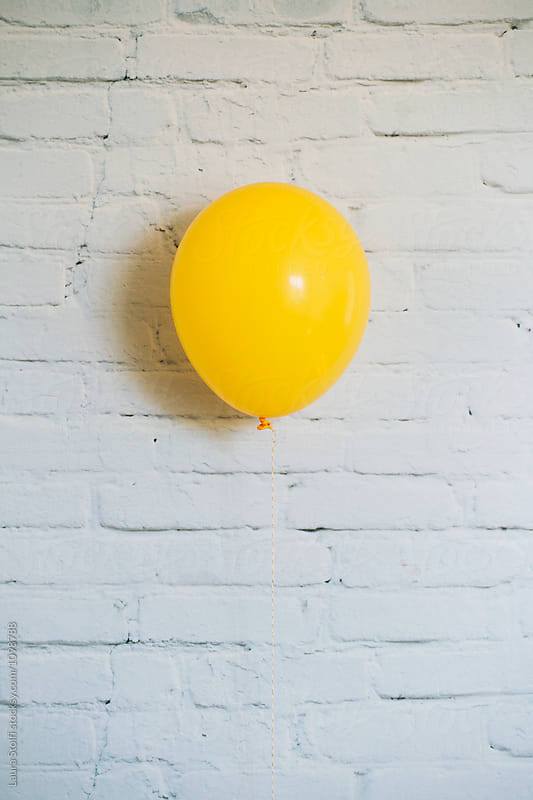 Yellow balloon floating in front of white bricks wall