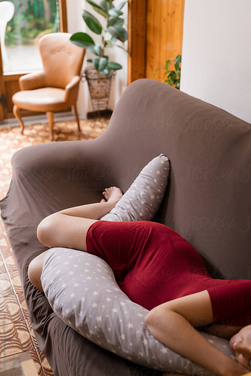 A pregnant woman lying on the sofa hugging a body pillow