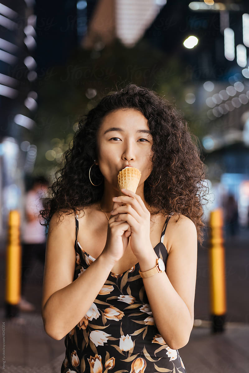 A woman eats icecream at night on the street