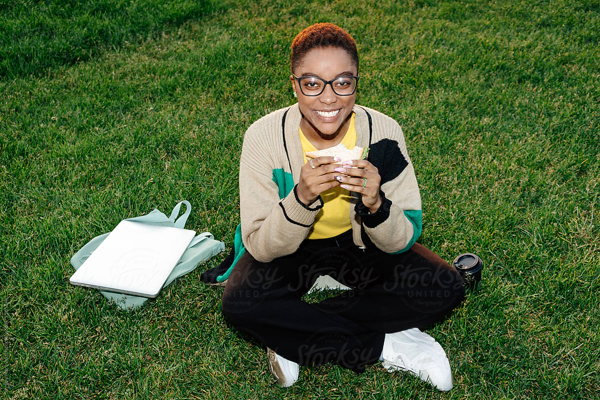 Smile female eating sandwich sitting on green lawn, direct flash