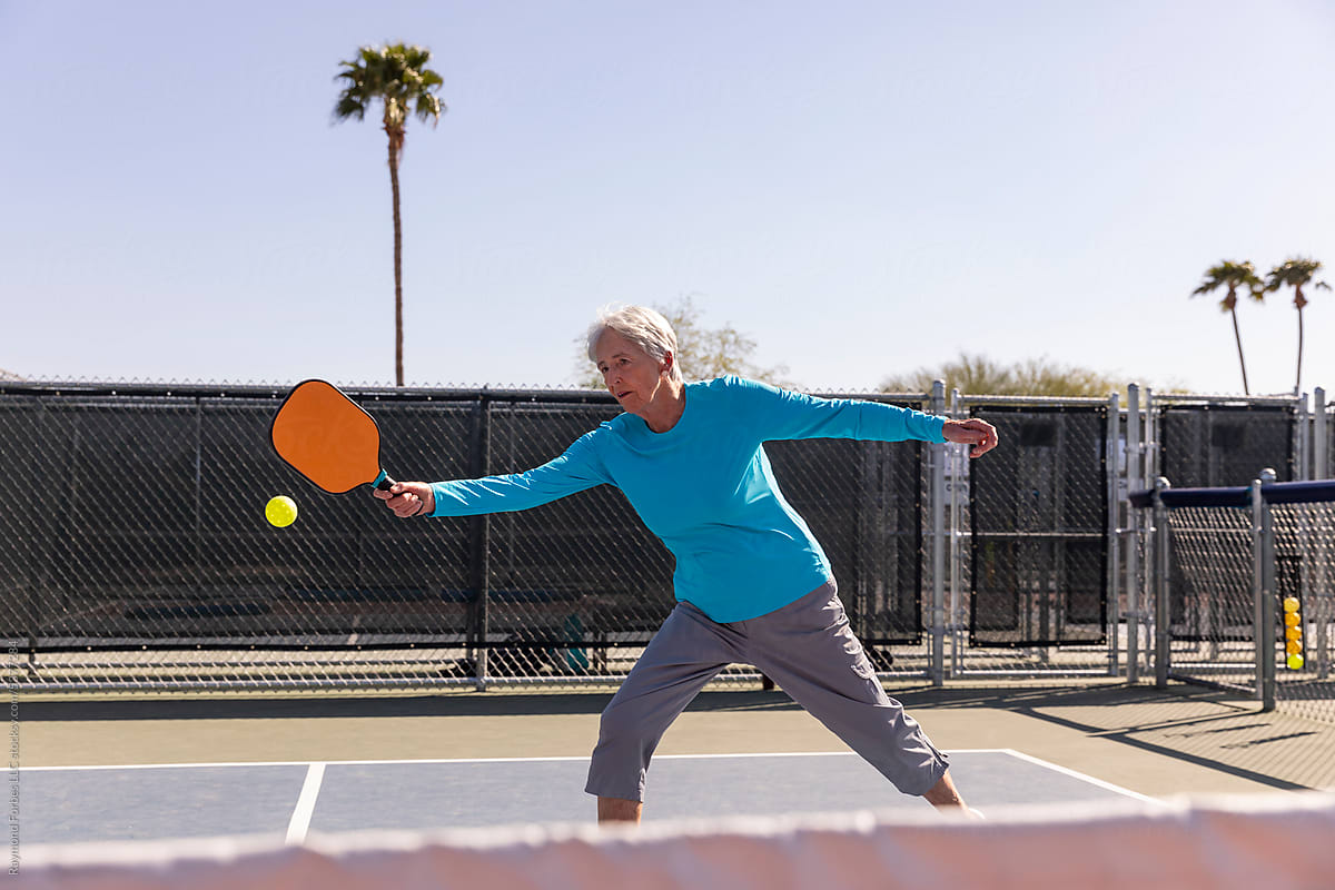 Senior Citizen Pickleball player on reaches to hit ball in match