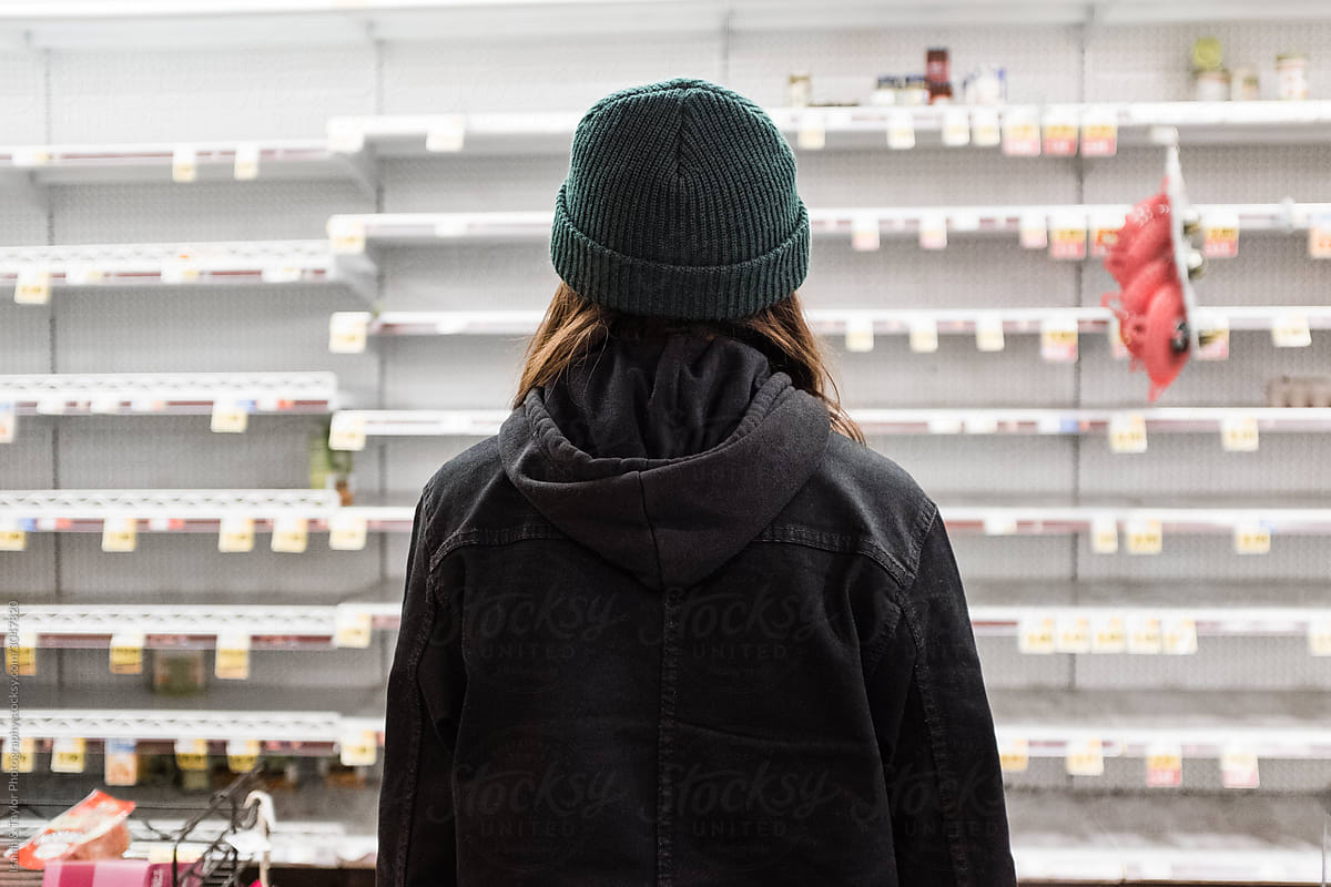 Person standing alone staring at empty grocery store shelves during the Coronavirus pandemic