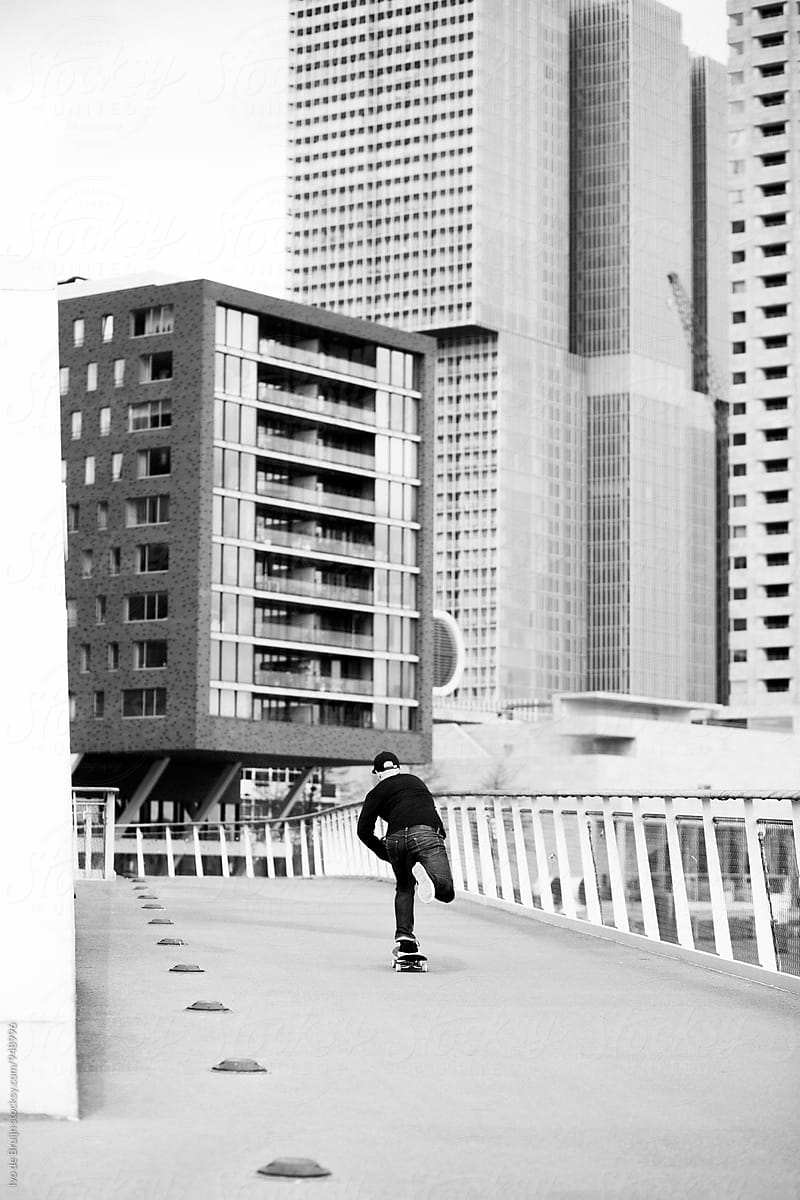 Skater riding on a bridge in the city, surrounded by skyscrapers or buildings. Photo in black and white