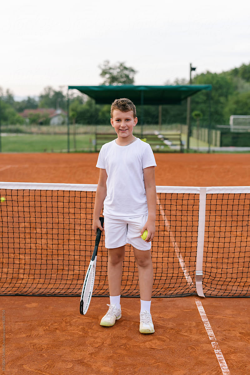 Young happy boy portrait standing on a tennis court