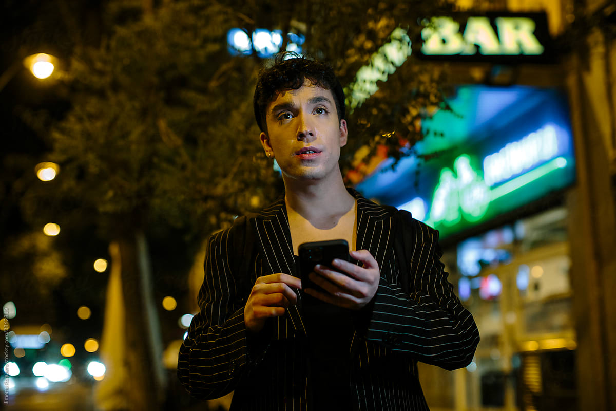 Young gen-z person at night in the city checking smart phone