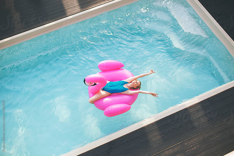 Beautiful young woman floating on a flamingo float in a swimming pool