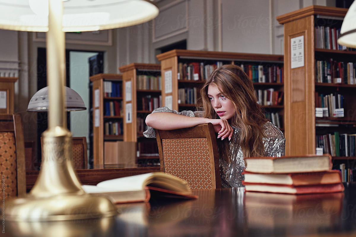 Young beautiful blonde misses a huge library at a table with books