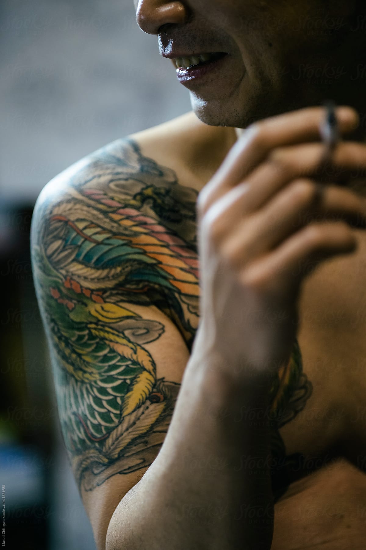 Smiling Japanese male with a cigarette in his hand and a tattoo on his right shoulder