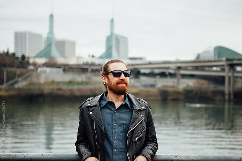 Hip man with red facial hair standing with cityscape behind him