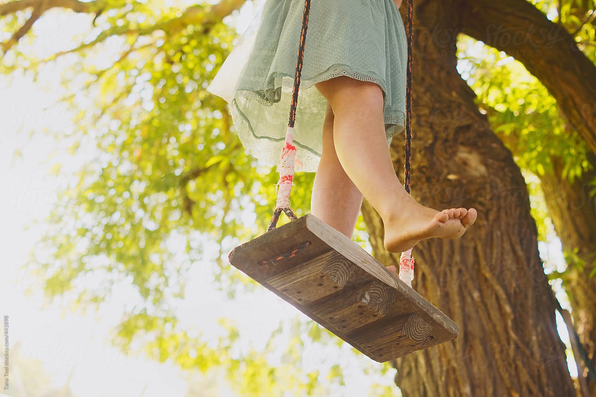 Young woman holds barefoot out while standing on wood swing