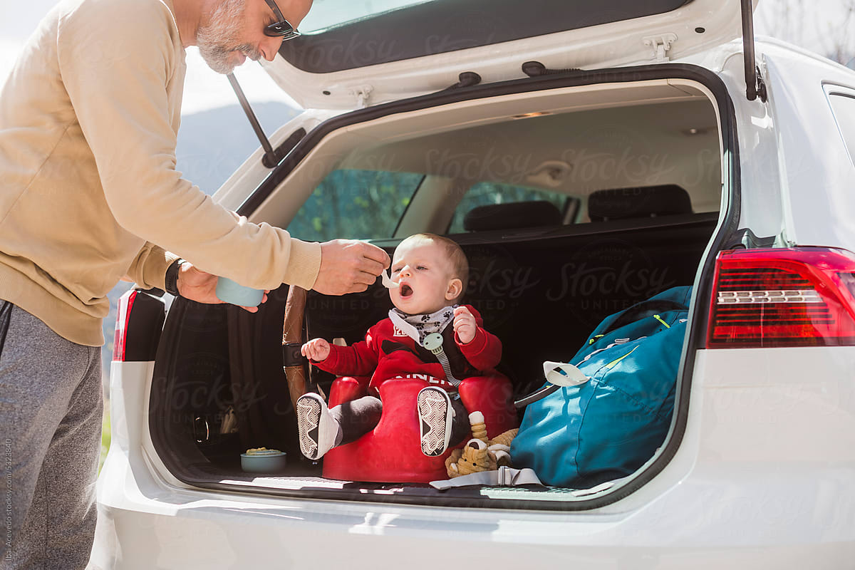 Standing father feeding newborn in car trunk