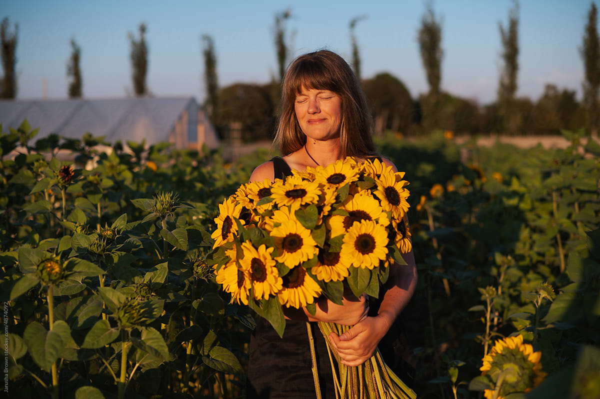 Woman in a summer dress stands in a sunflower field at sunset.