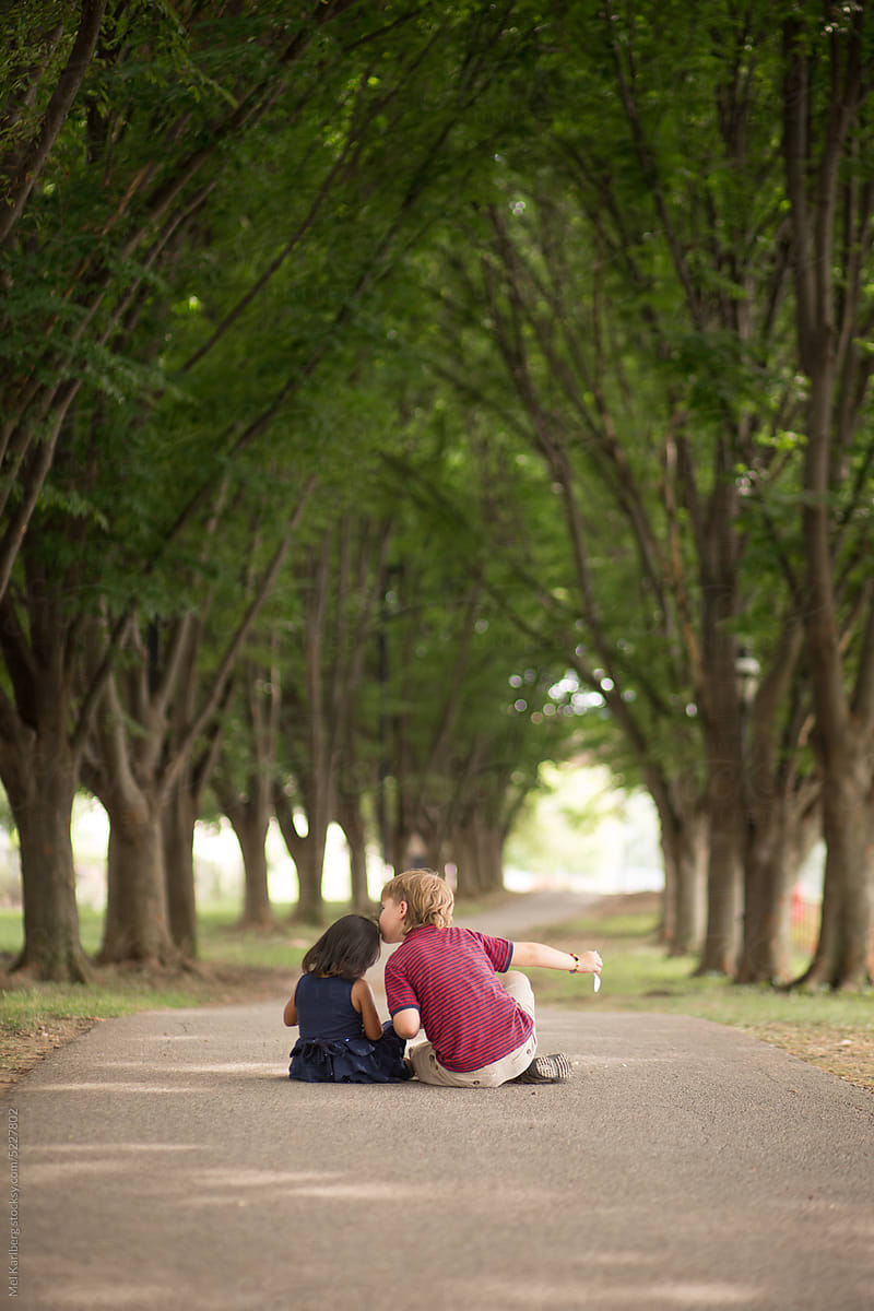 Boy and girl sitting on tree lined path