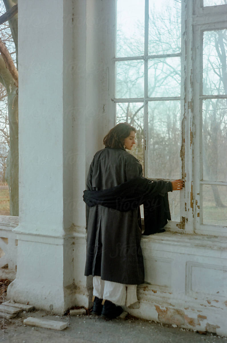 portrait of a woman in a black raincoat standing by the window