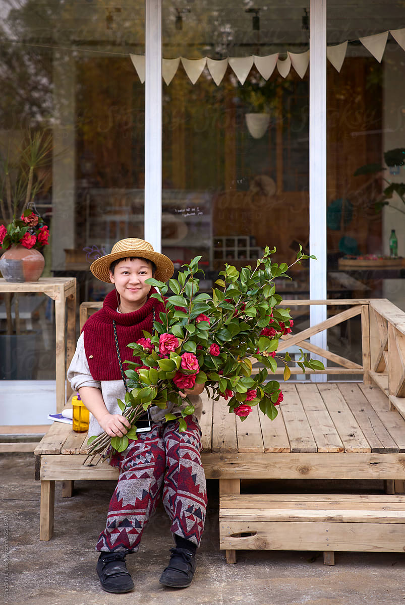 Asian woman holding fresh camellia flowers and sitting on wooden bed