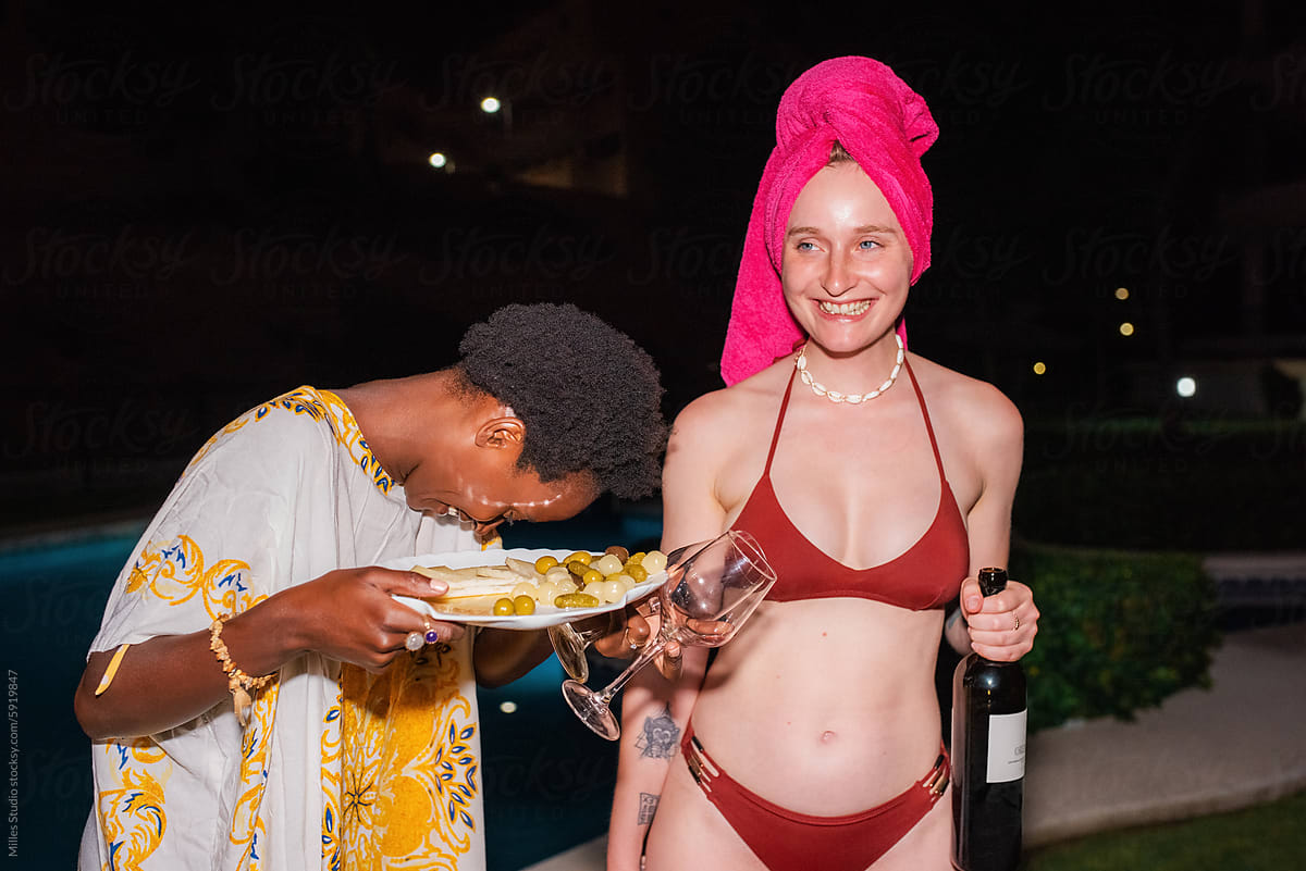 Two young women sincerely laughing at joke near pool at night