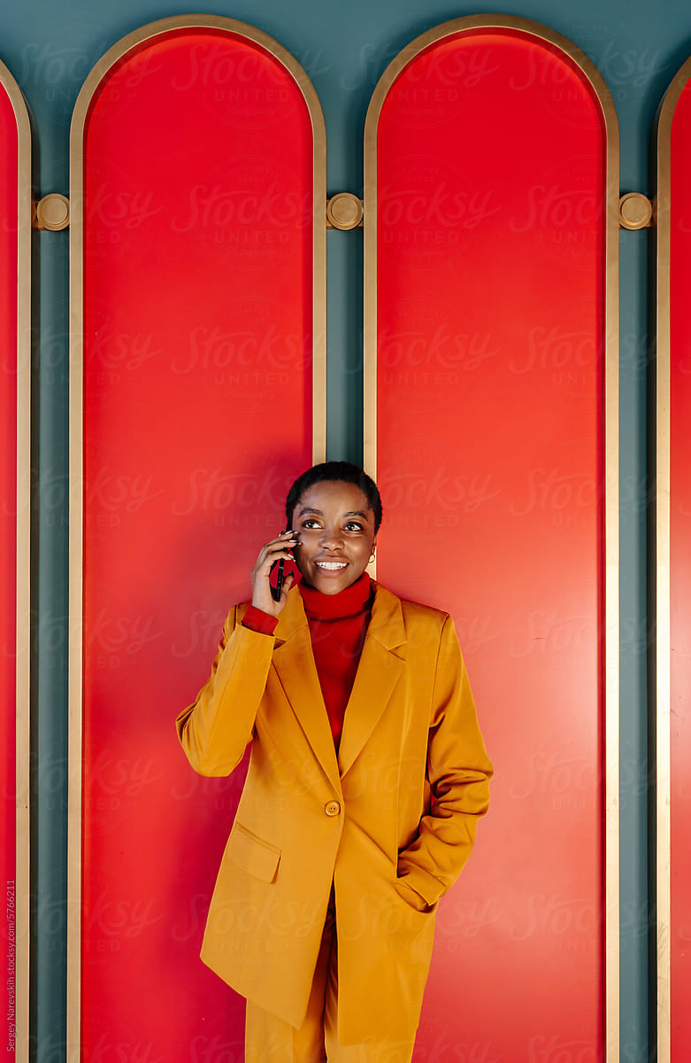 Business woman in yellow suit having phone call against red panels