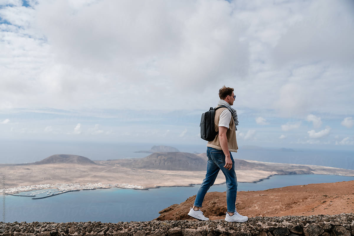 Man with backpack on hill with view on island in ocean.