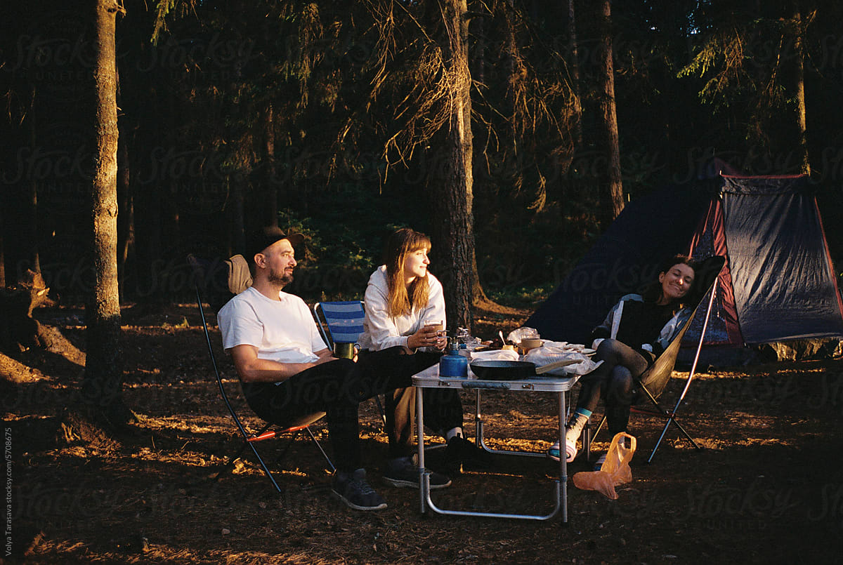 Three friends relaxing on camp chairs near the tent