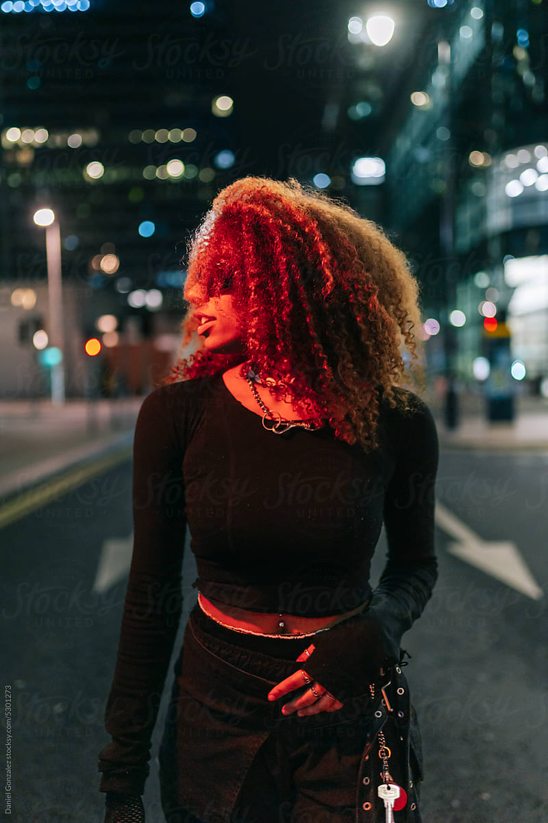 Woman with curly hair standing on city street at night