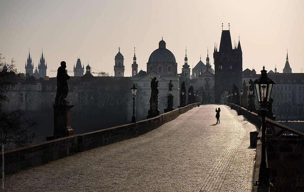 A tourist takes a photo on an empty bridge in Prague.