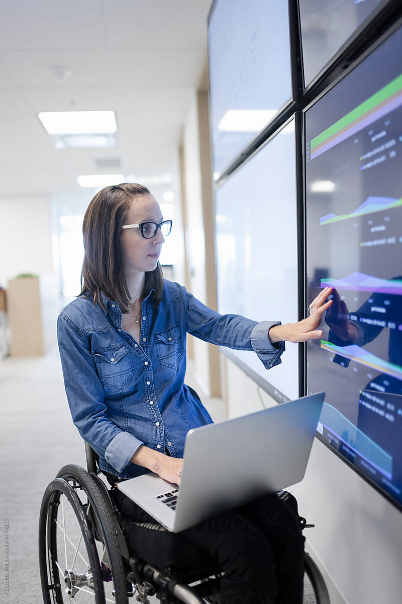 Analyst in wheelchair reading statistics on digital screen.
