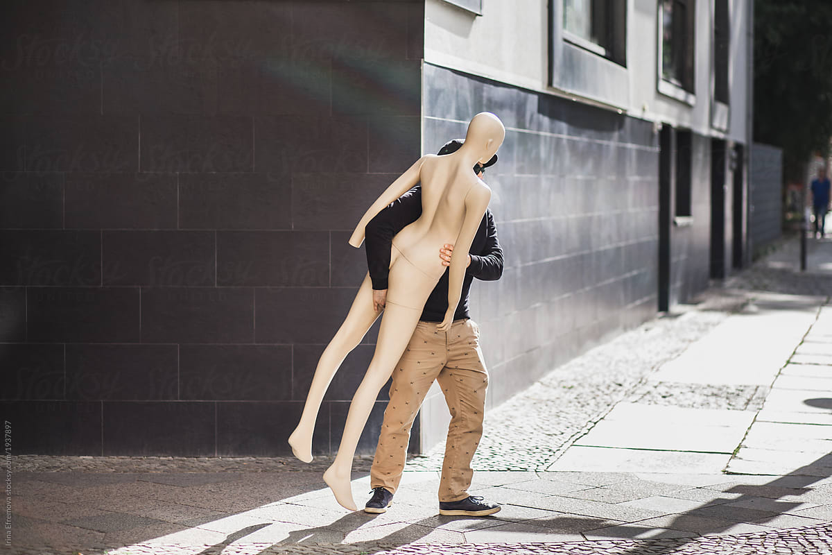 Man on a street carrying an artificial woman