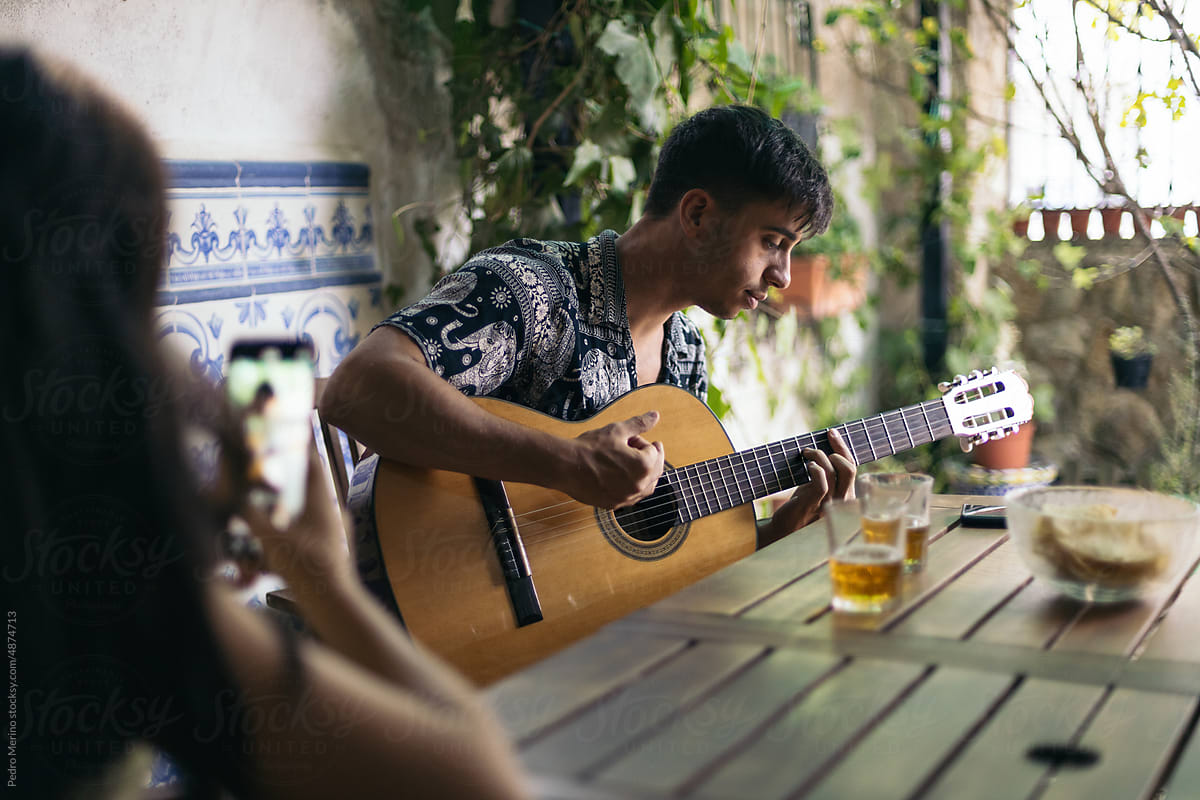Man playing the Spanish guitar outdoors while his friend records him