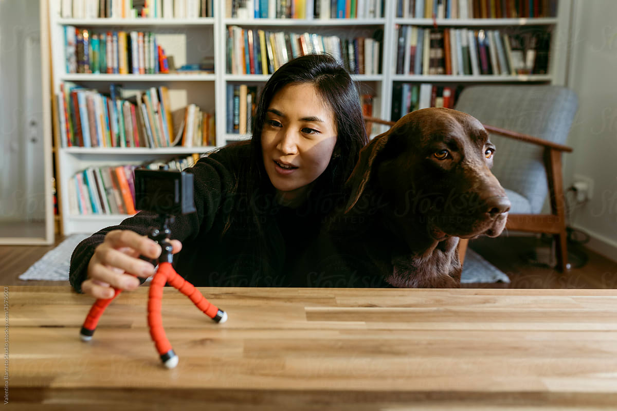 female east asian woman and her labrador dog at home recording a video