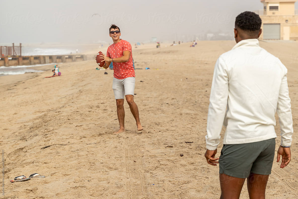 Boys Throw A Football At the Beach