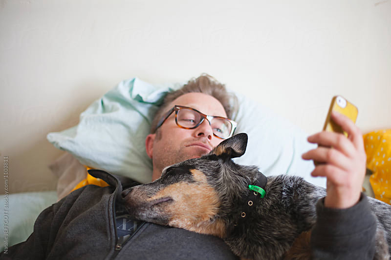 Middle aged man on his bed with his blue heeler dog