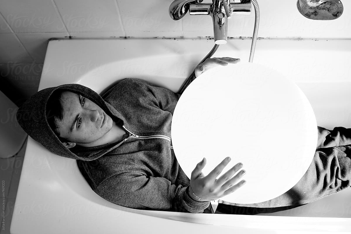 Teenager wearing clothes in a bath and holding spherical object.