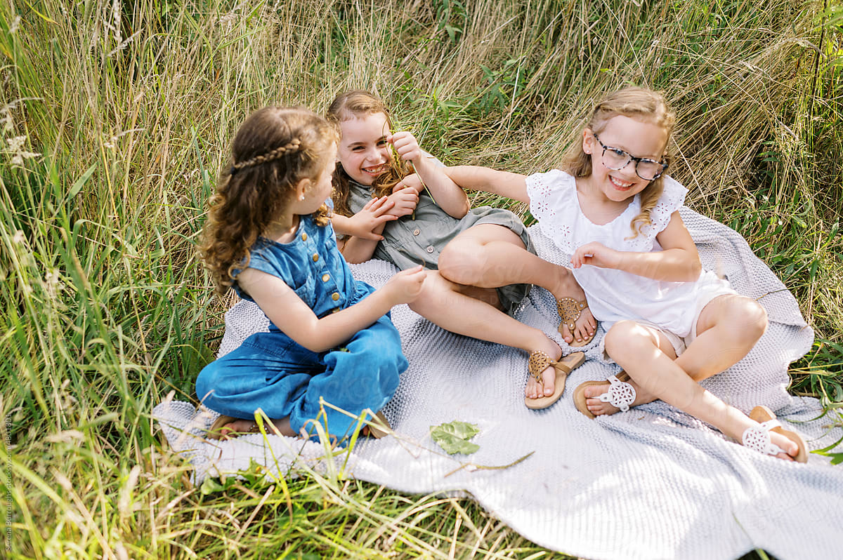 Three sisters laughing and playing together on a blanket in a field