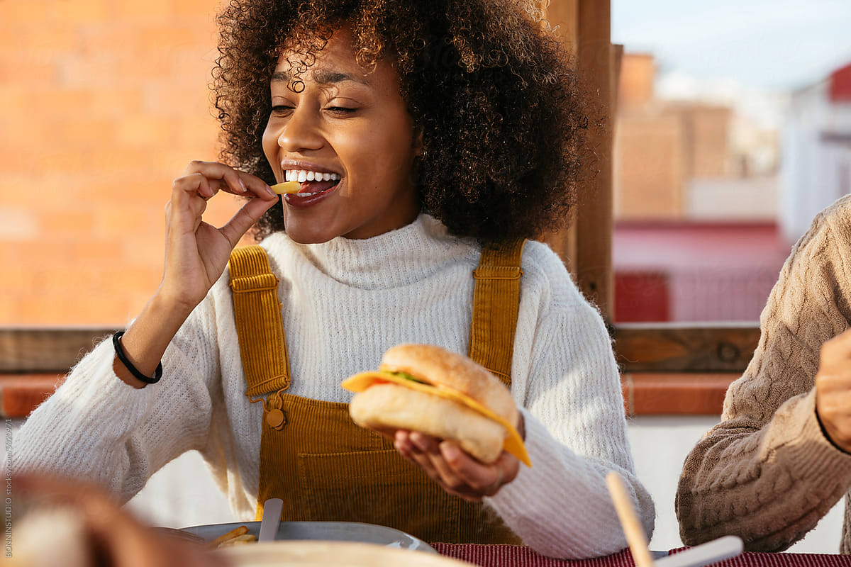 Cheerful woman eating burger in a rooftop