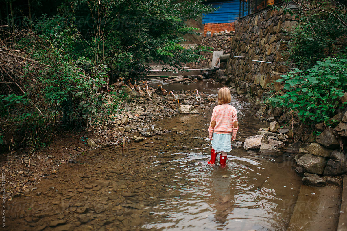 A little girl wades in a stream near a rock wall