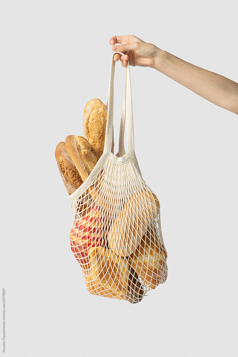 Hand holds net bag with bread.