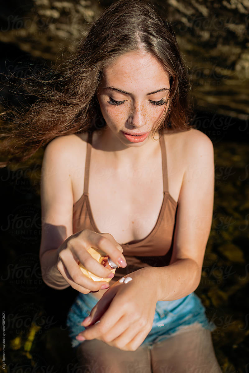 Summer portrait of young woman with freckles using sunscreen