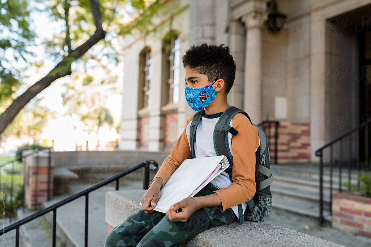 Young Boy Wearing a Mask and Holding His Books Waits After School