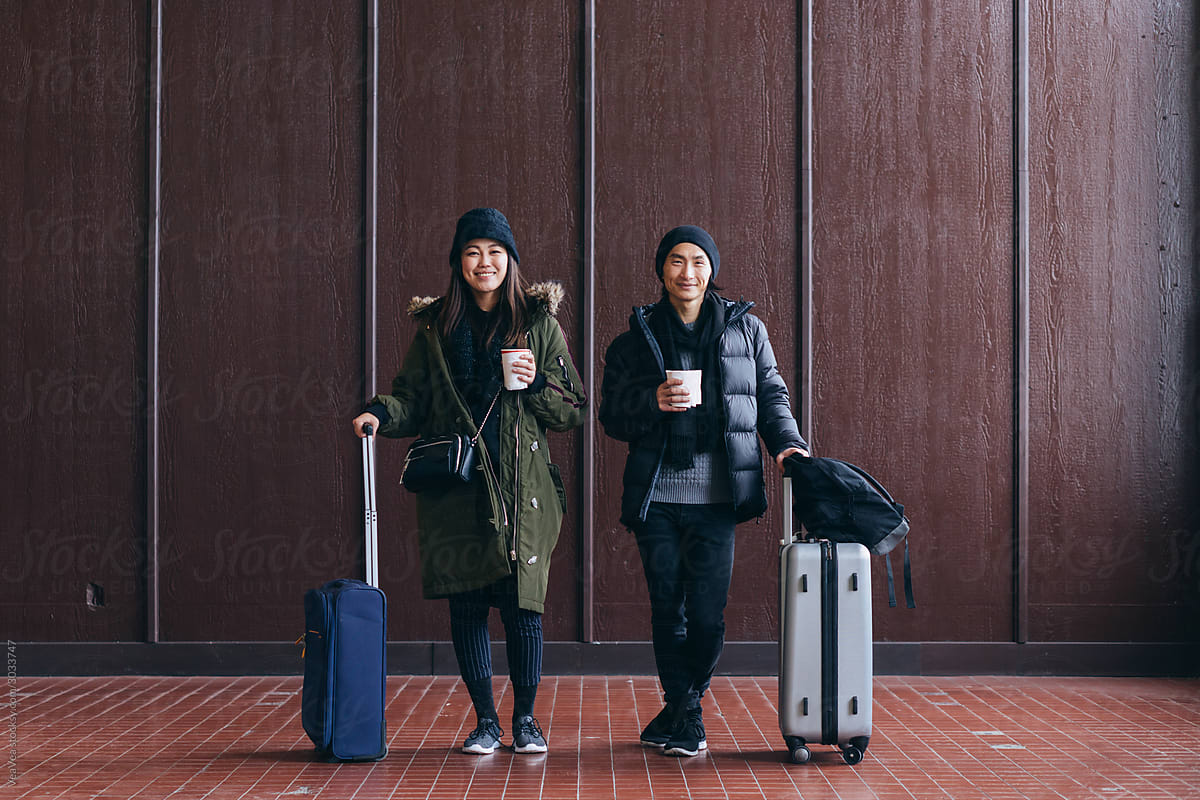 Beautiful Asian couple posing with suitcases indoor