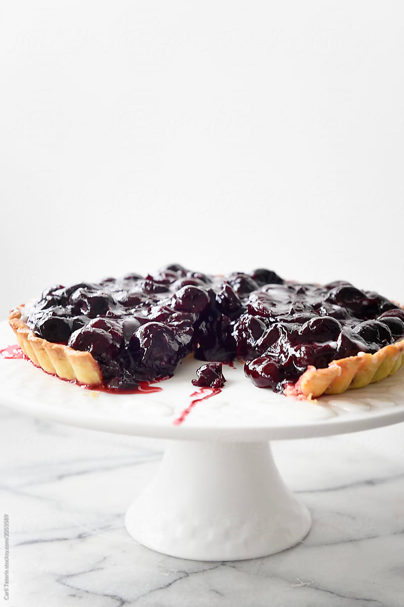 Cherry tart with a slice removed on a white cake stand