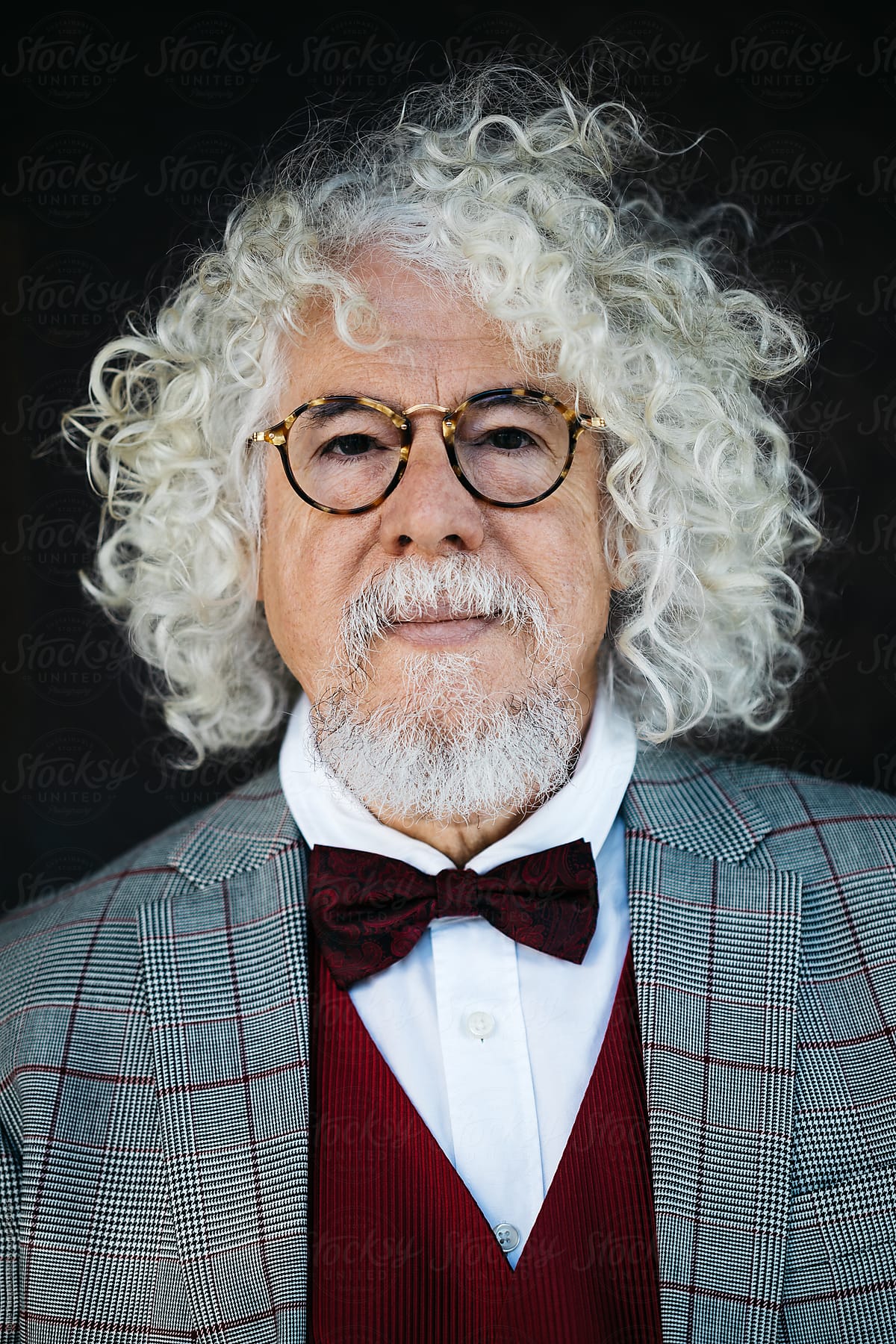 Elegant man with white curly hair in glasses.