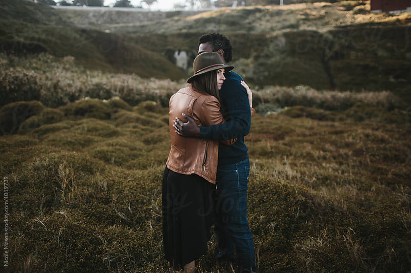attractive couple hugs in field of dark green grass