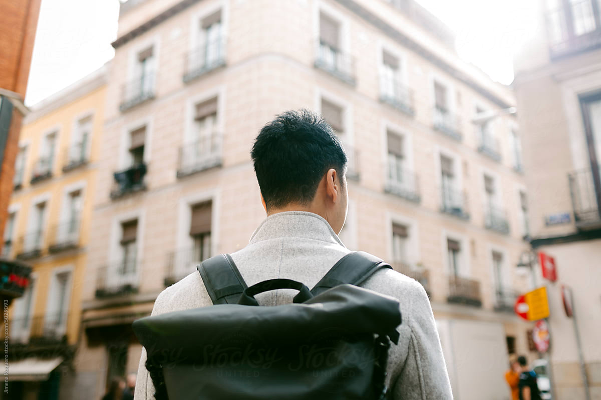 Back of young stylish man carrying a backpack in sunlight in the city