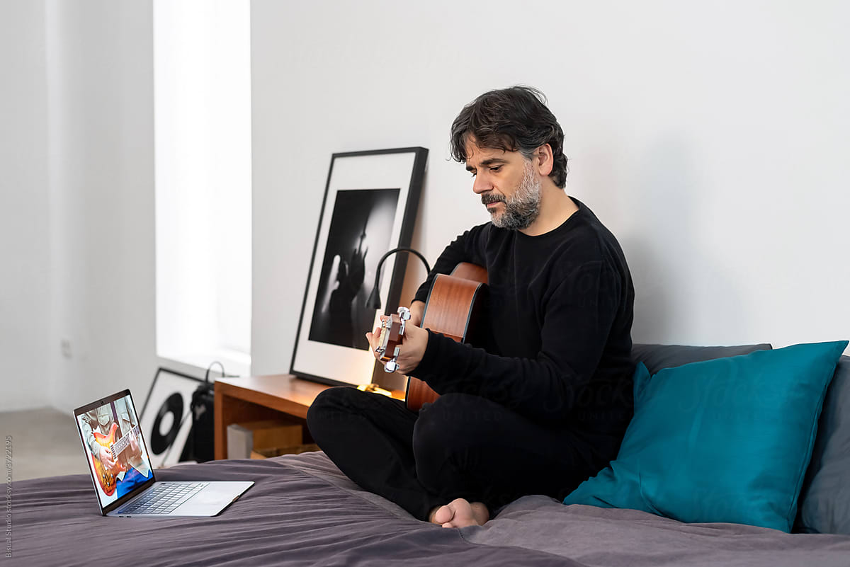 Focused man with laptop playing guitar in bedroom